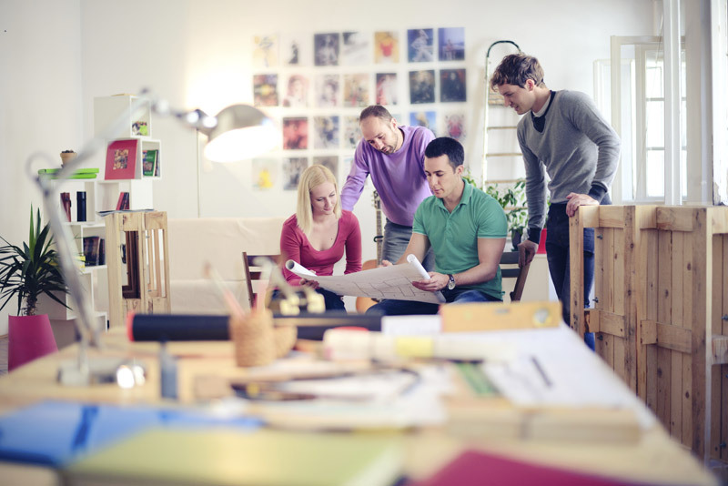 Group of 4 creative professionals reviewing plans on paper.