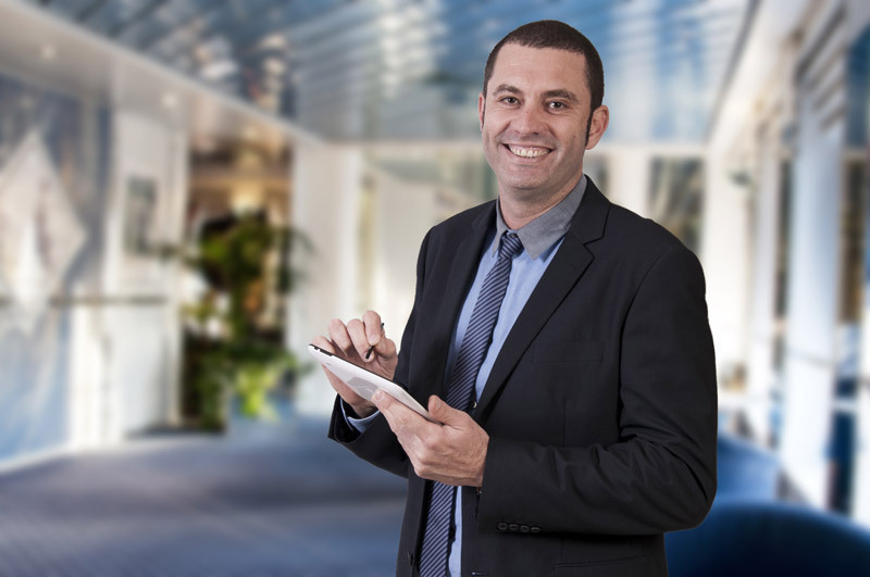 Smiling man in suite checking off items on a clipboard he's holding.