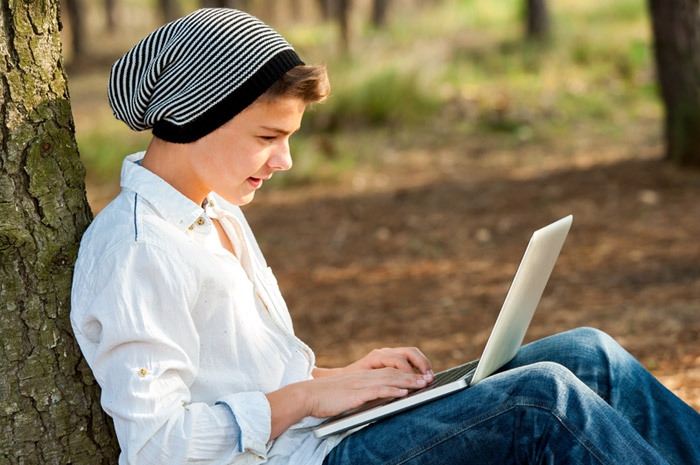 Young man sitting in a park working on a laptop.